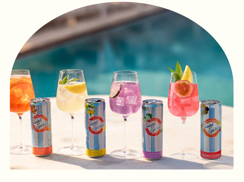 Five colorful Saint Spritz wine spritzes in glasses alongside Amalfi, Sicily, Hugo, and Sardinia cans by the pool