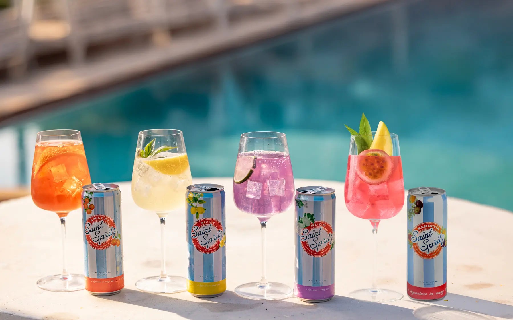 Five colorful Saint Spritz wine spritzes alongside Amalfi, Sicily, Hugo, and Sardinia cans by the pool